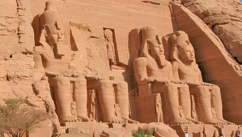 The grand facade of Abu Simbel Temple, featuring colossal statues of Pharaoh Ramses II carved into the sandstone cliffs, with a clear blue sky above.