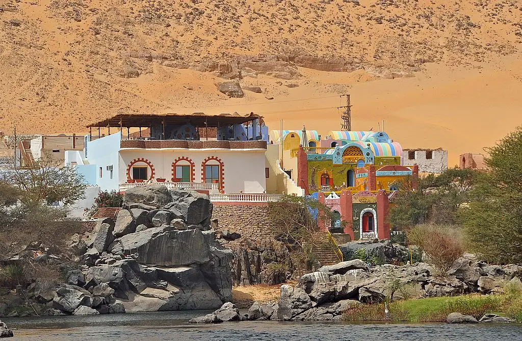 A Nubian village by the Nile River, showcasing traditional mud-brick houses, colorful decorations, and locals dressed in vibrant clothing.