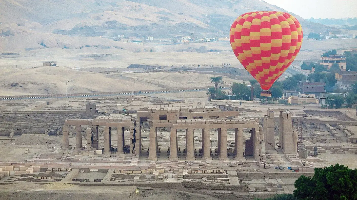 A hot air balloon soaring over the Luxor skyline at sunrise, offering a bird’s eye view of the ancient temples, the Nile River, and surrounding desert landscape.