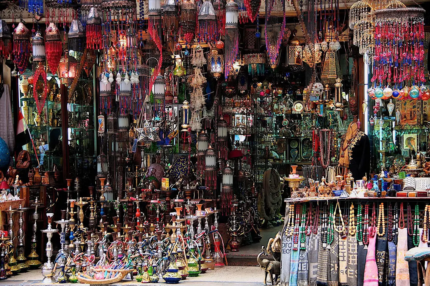 A bustling street in El Quseir city with colorful market stalls, local shops, and tourists browsing for souvenirs under the bright sun.