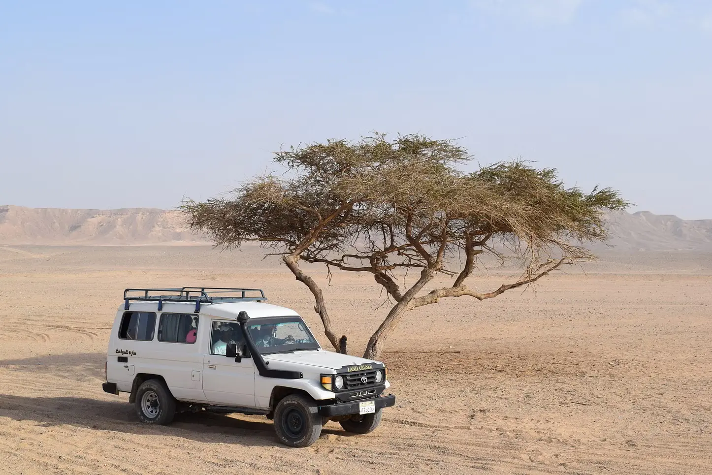 A rugged 4x4 vehicle navigating the golden sand dunes of the Marsa Alam desert, with a dramatic sunset painting the sky in warm hues.